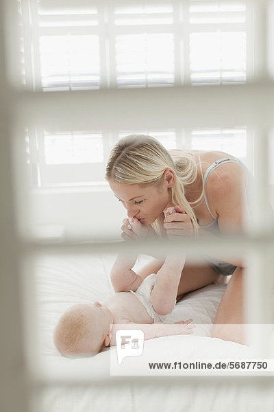 Mother kissing babys feet on bed