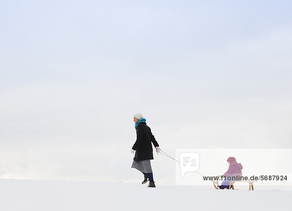 Mother pulling daughter on sled in snow