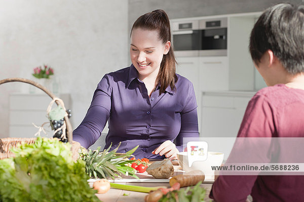 Women eating vegetables in kitchen