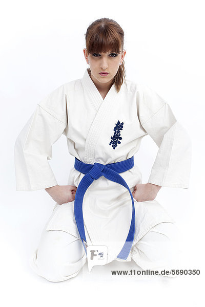 Junge Frau kniet im Karate-Gewand mit blauem Gürtel
