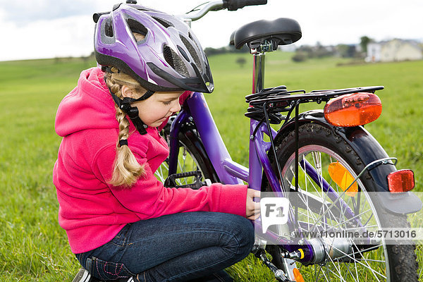 Mädchen mit Fahrradhelm  überprüft etwas am Fahrrad