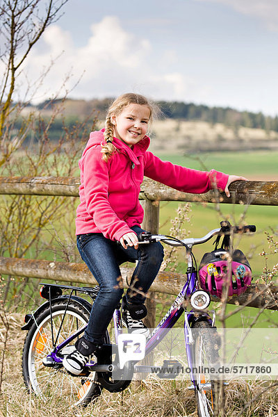 Girl with her bicycle in front of rural landscape