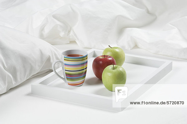 Tablett mit Tee und Äpfeln auf dem Bett zum Frühstück  Nahaufnahme