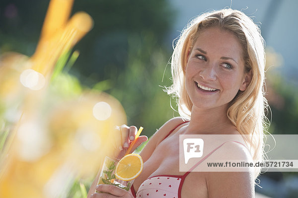 Österreich  Salzburger Land  Junge Frau mit Getränk am Pool