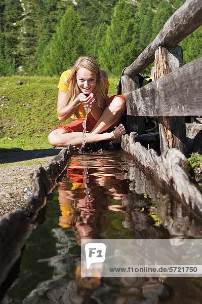 Österreich  Salzburger Land  Junge Frau trinkt Wasser aus Wassertrog  Portrait