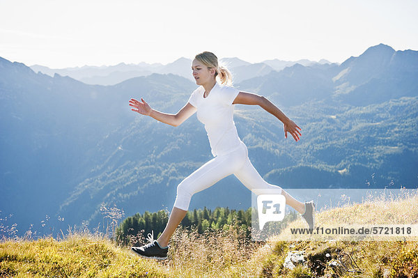 Austria  Salzburg County  Young woman running and jumping in alpine meadow