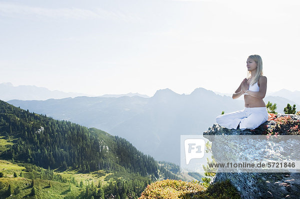 Österreich  Salzburger Land  Junge Frau auf Felsen sitzend und meditierend
