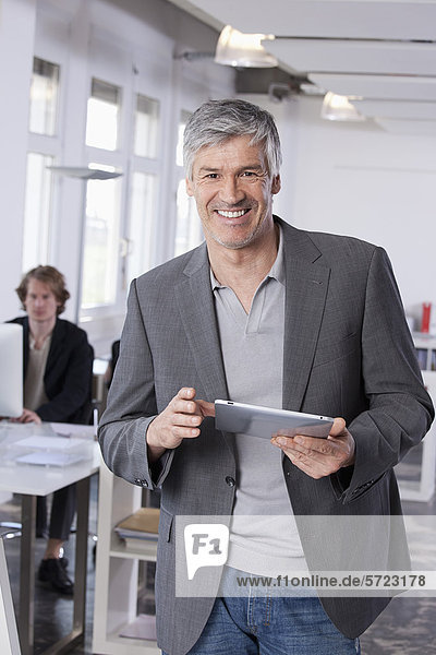 Mature man using digital tablet  colleague working in background