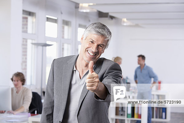 Mature man showing thumbs up  colleagues in background