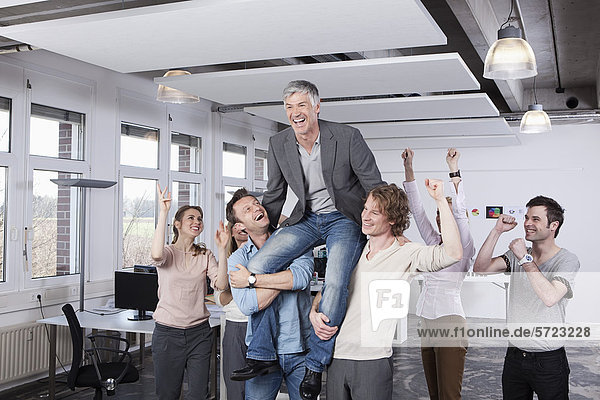 Colleagues carrying mature man on shoulder  smiling