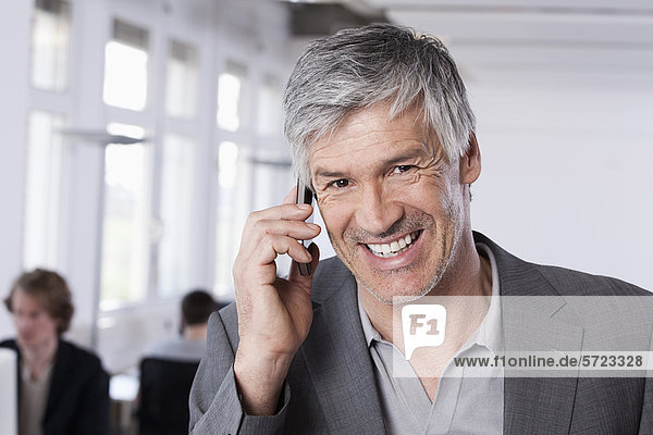 Mature man on mobile phone  colleagues working in background