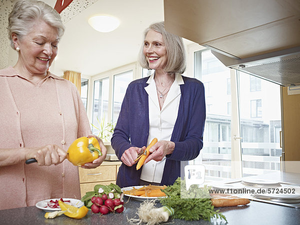 Seniorinnen schneiden Gemüse im Pflegeheim  lächelnd