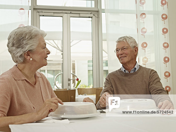 Deutschland  Köln  Seniorenpaar am Tisch sitzend  lächelnd
