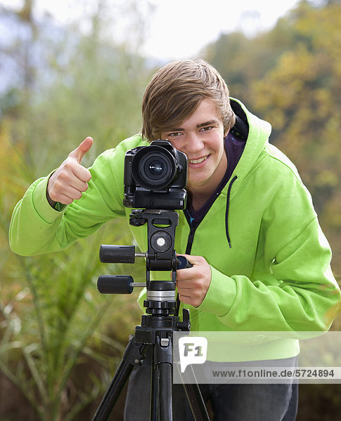 Österreich  Junger Mann mit Kamera  lächelnd  Portrait
