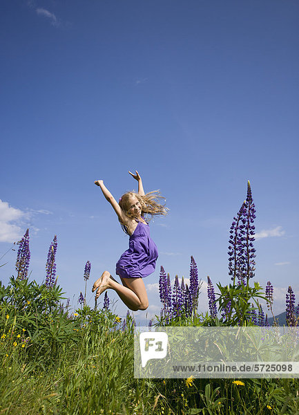 Österreich  Teenagerin im Lupinenfeld springend  lächelnd  Portrait