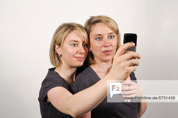 Zwillingsschwestern fotografieren sich selbst mit einem Handy