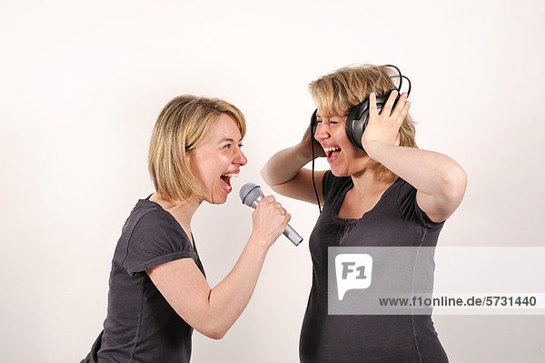 Zwillingsschwestern  eine schreit in ein Mikrophon  die andere hat Kopfhörer auf und hält sich die Ohren zu