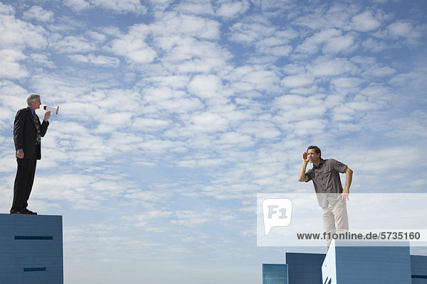Überdimensionale Männer  die auf Dächern stehen  einer spricht durch ein Megaphon.