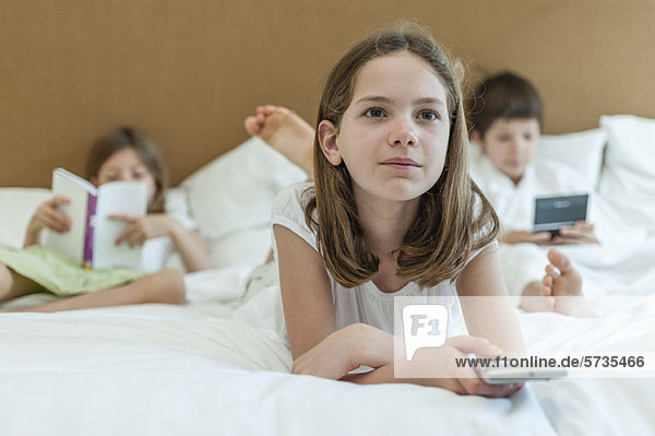 Girl lying on bed watching TV  siblings in background