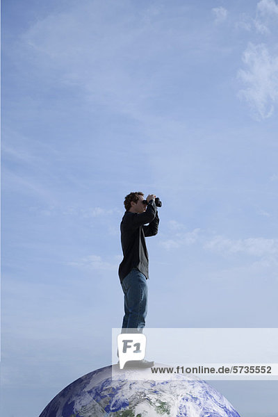 Mann  der auf dem Dach der Welt steht und durch ein Fernglas schaut.