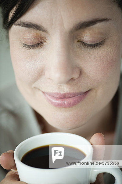 Mittlere Erwachsene Frau riecht eine Tasse Kaffee.