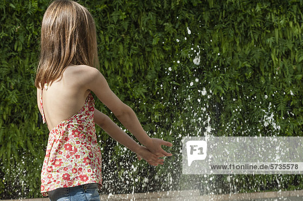 Mädchen spielt im Wasser im öffentlichen Brunnen  Rückansicht