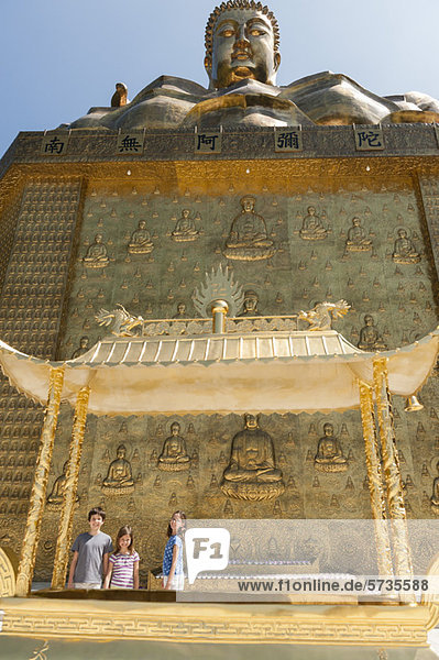 Junge Touristen stehen unter einer großen Buddhastatue.