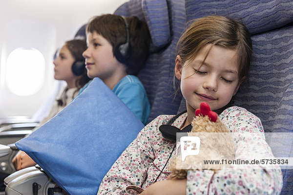 Mädchen schläft im Flugzeug mit Plüschtier