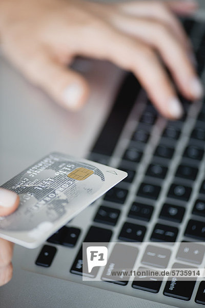 Woman holding credit card while using laptop computer  cropped