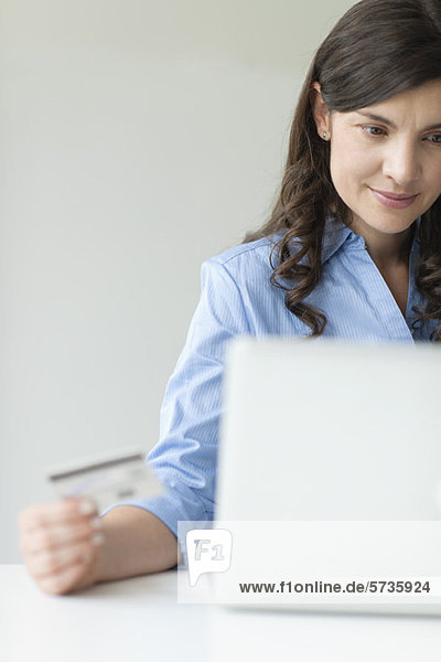 Mid-adult woman holding credit card while using laptop computer