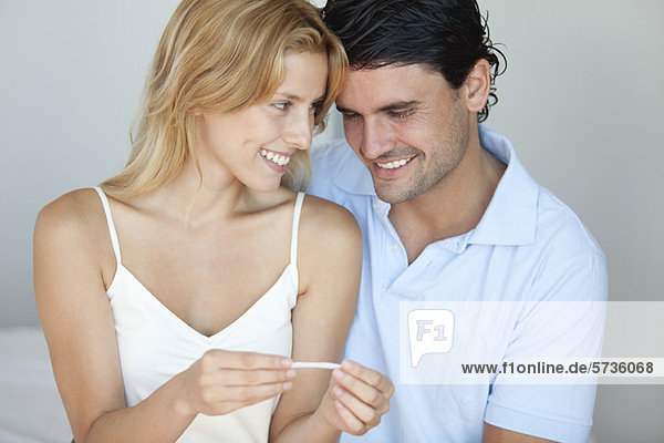 Paar schaut auf Schwangerschaftstest  lächelnd