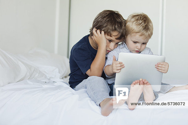 Young brothers sitting on bed looking at digital tablet