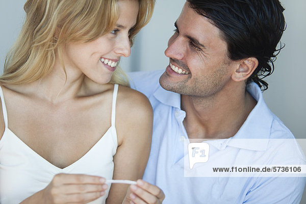 Paar lächelt sich an  Frau mit Schwangerschaftstest