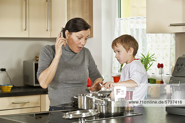 Frau telefoniert beim Kochen  Junge treibt Unfug