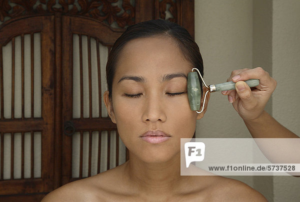 Woman receiving facial massage with jade rollers                                                                                                                                                    