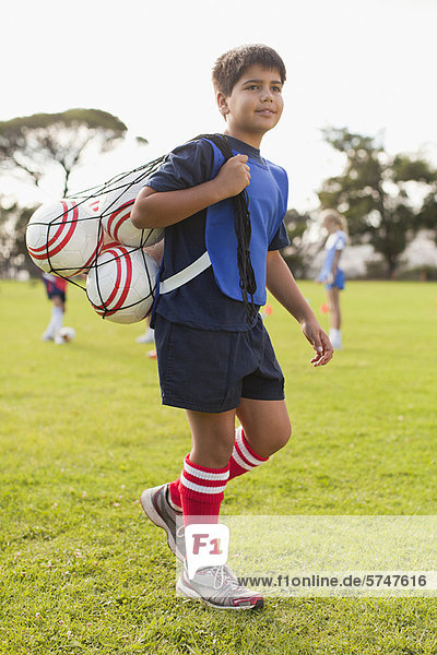 Junge trägt Fußbälle auf dem Spielfeld