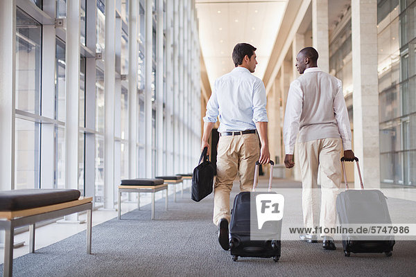 Businessmen rolling luggage in hallway