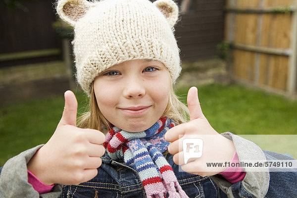 Smiling girl giving thumbs-up outdoors