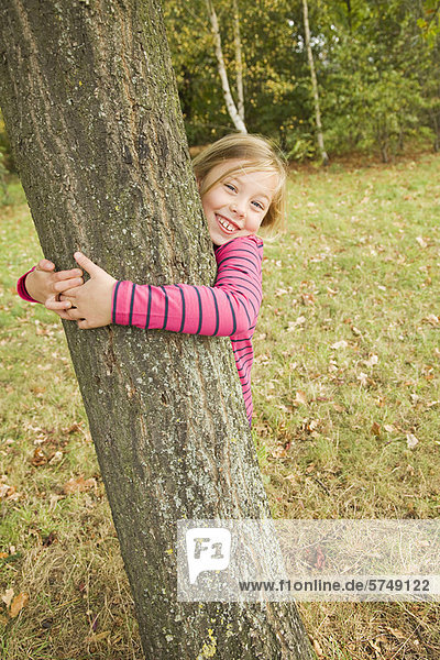 Lächelndes Mädchen umarmt Baum im Freien