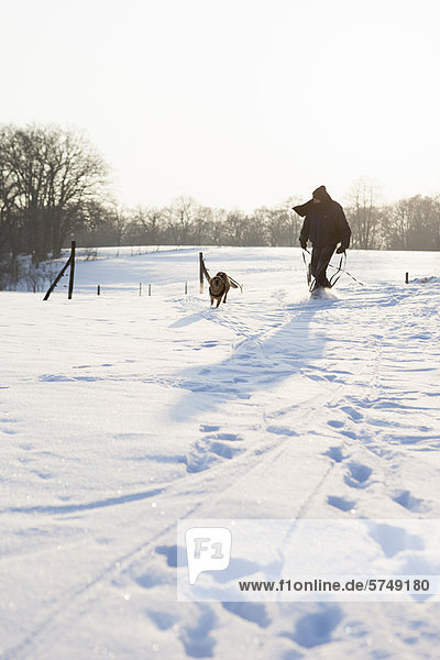Mann spazierengehender Hund im Schneefeld