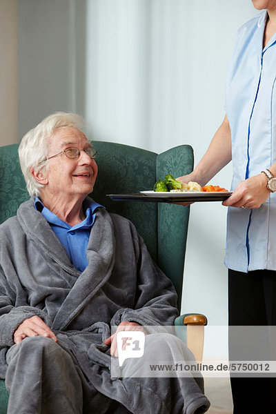 Betreuerin bringt Essen zu einem älteren Mann