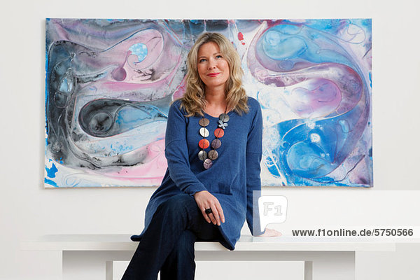 Frau mittleren Alters sitzt vor Öl-Malerei in der Galerie