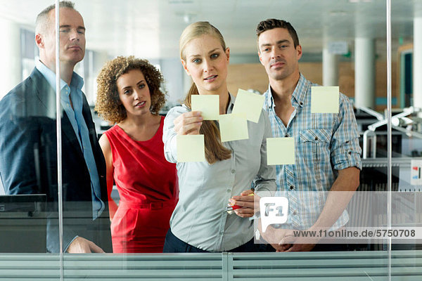 Office colleagues arranging adhesive notes on office window