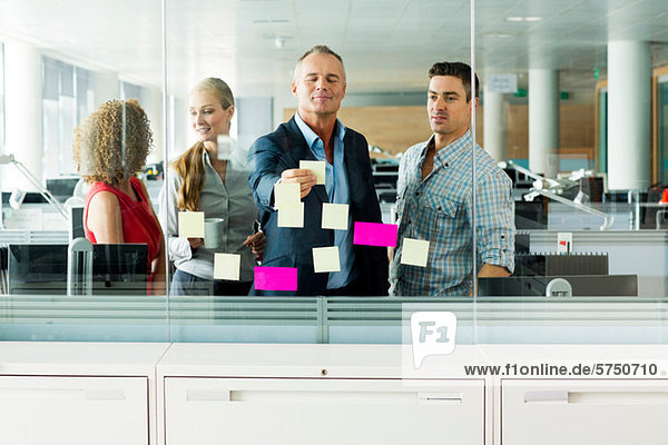 Office colleagues arranging adhesive notes on office window