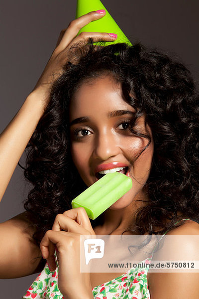 Junge Frau isst grünes Eis und trägt einen Partyhut  Porträt