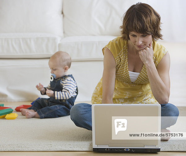 Mother using laptop while baby plays