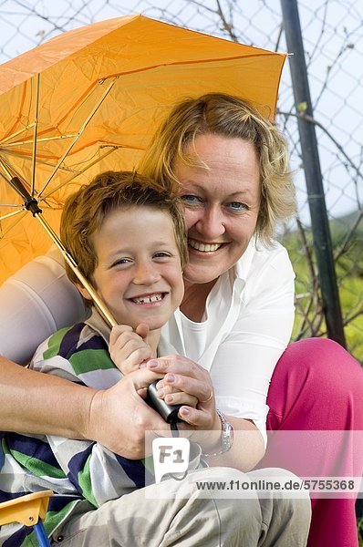 Mutter und Sohn sitzen unter dem Regenschirm