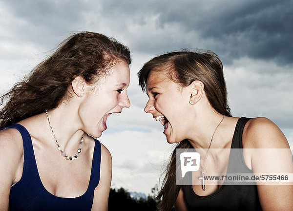 Two teenage girls screaming at each other  in front of storm clouds