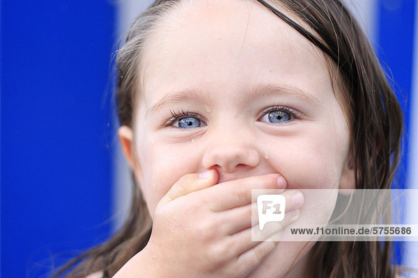 Dreijähriges Mädchen hält sich lachend den Mund zu