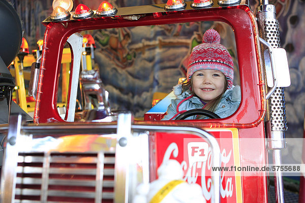 Dreijähriges Mädchen fährt Autokarusell auf dem Weihnachtsmarkt